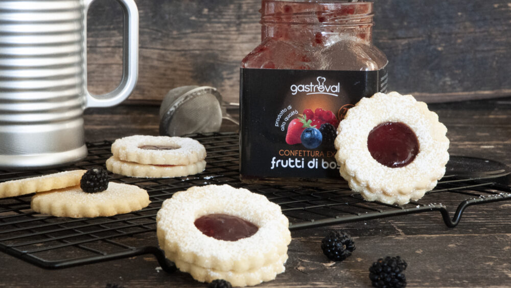 biscotti disposti sul piano da lavoro e vasetto di confettura frutti di bosco aperto